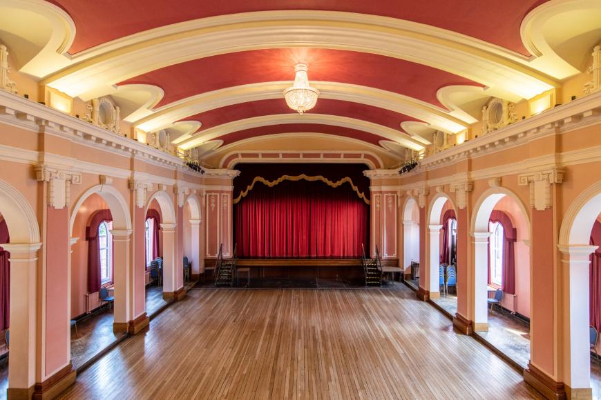  View from the single tiered balcony overlooking the sprung flat floor ballroom. Apron stage. Proscenium arch. Barrel vault ceiling. 